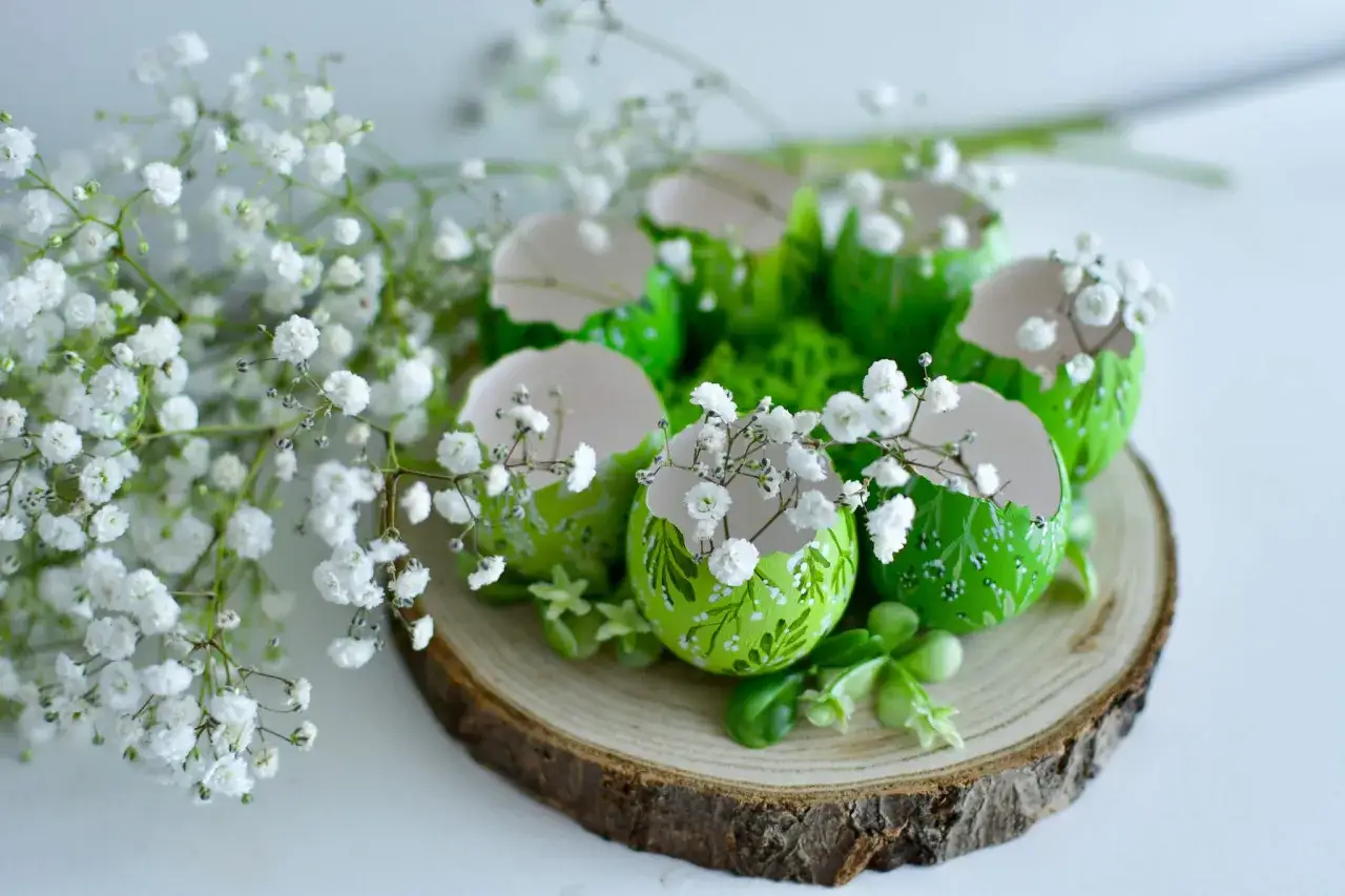 Zielone, ozdobione jajka z gipsówką i zielenią na plastrze drewna. Inspiracja, jak zrobić stroik wielkanocny.