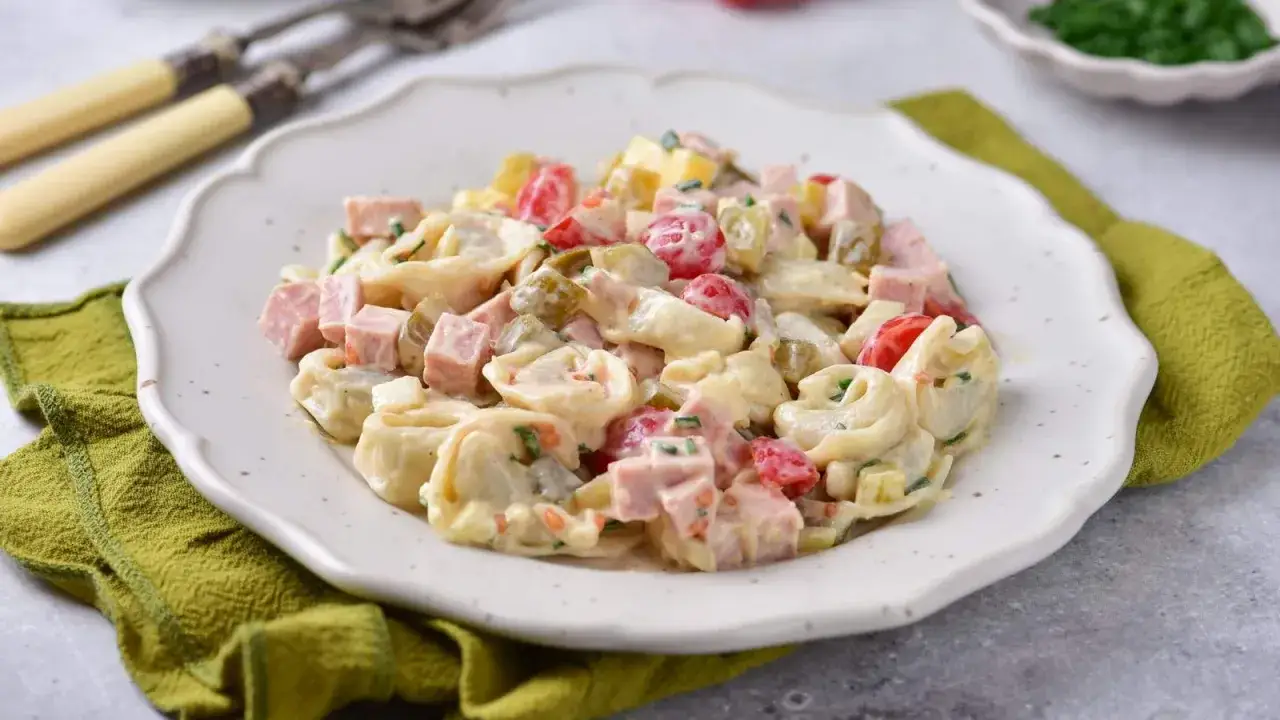 Sałatka z tortellini, szynką, pomidorkami i ogórkiem konserwowym w kremowym sosie.