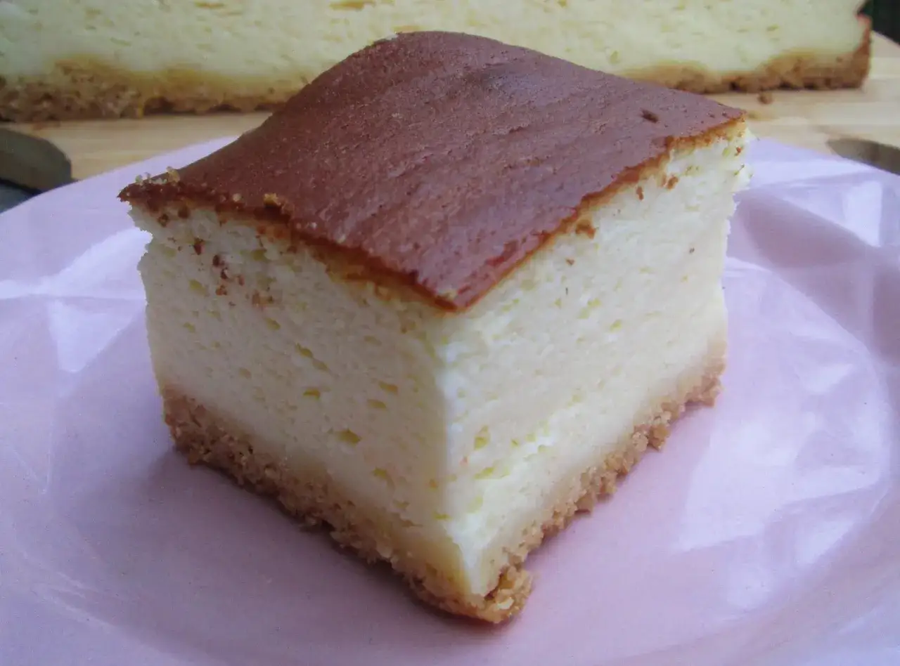 Idealny sernik z wiaderka który nie opada, z chrupiącym spodem i puszystym wnętrzem, na różowym talerzu.