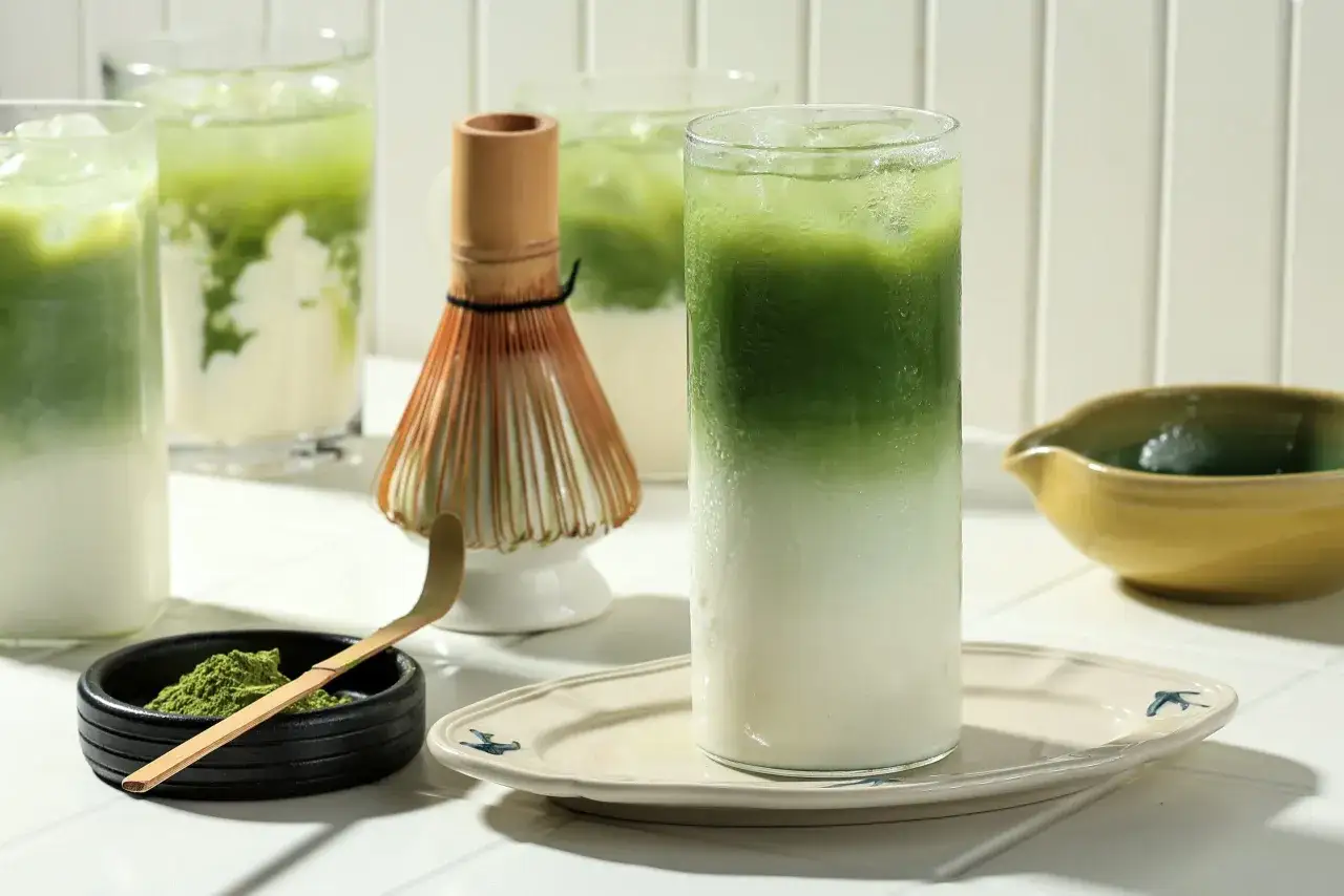 Zielone napoje matcha z lodem, bambusowa miotełka i proszek matcha.