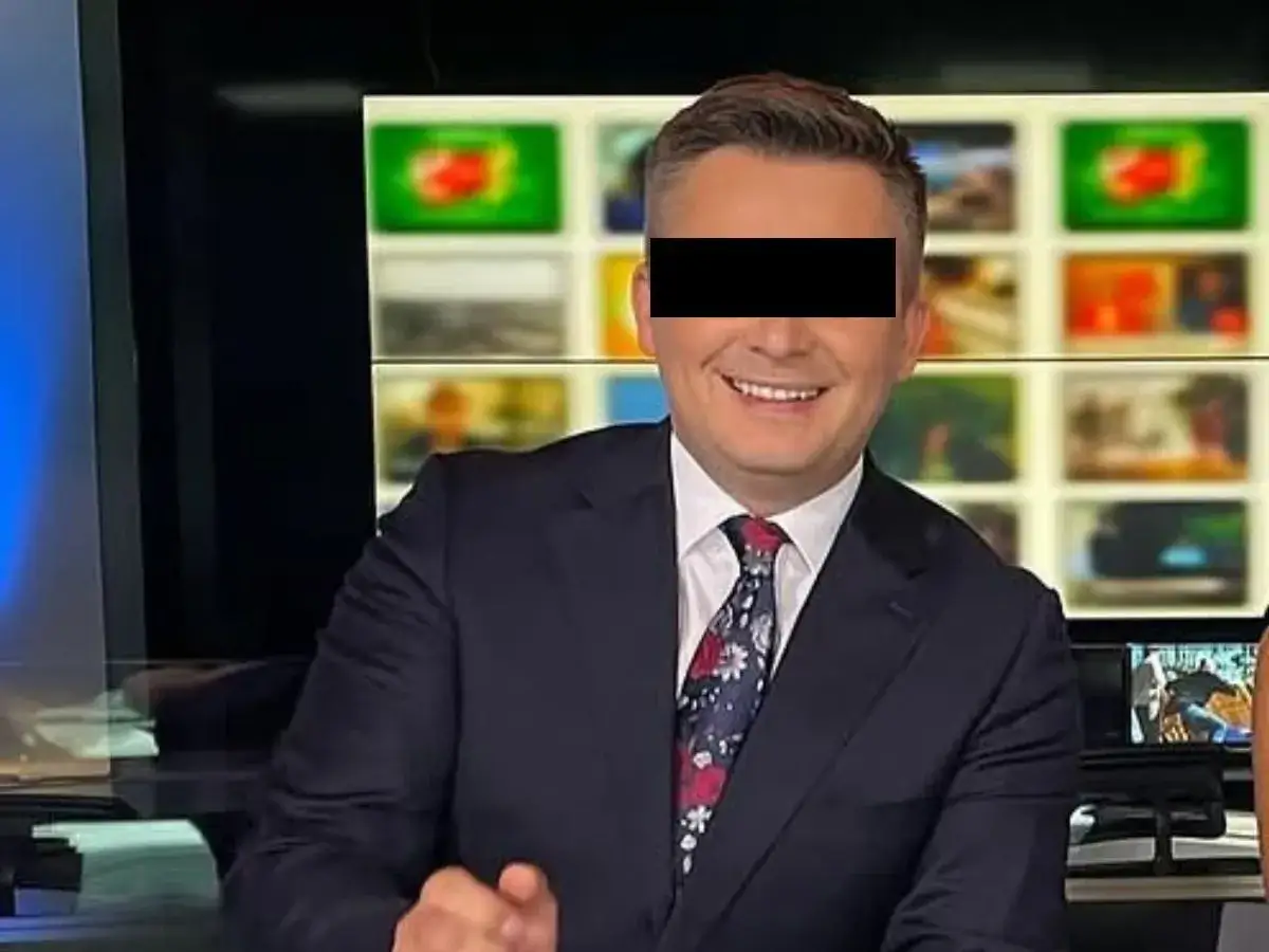 Uśmiechnięty mężczyzna w garniturze, z zasłoniętymi oczami, siedzi przed ekranami w studiu TVN. To Mateusz Walczak.
