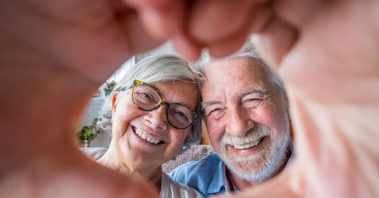 Uśmiechnięta para seniorów tworzy serce z dłoni. Ich twarze promieniują radością i miłością, która trwa przez lata.