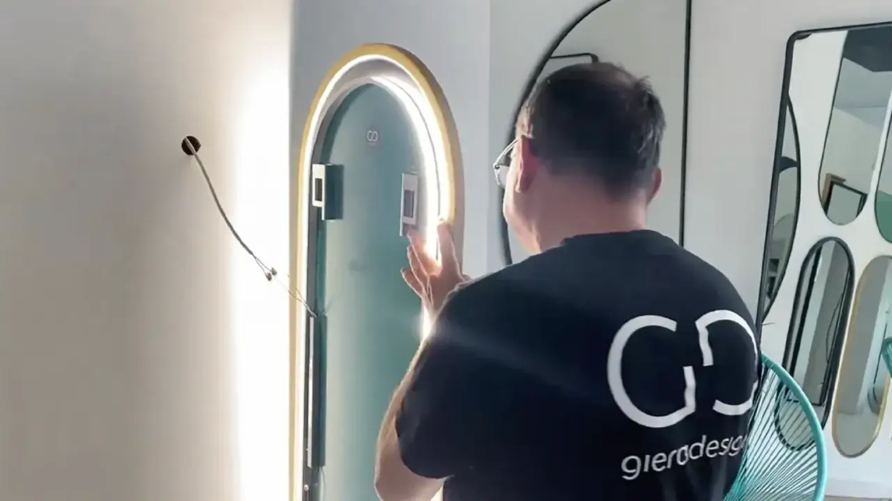 Mężczyzna montuje lustro z oświetleniem LED. Widać przewód wychodzący ze ściany, przygotowany do podłączenia.