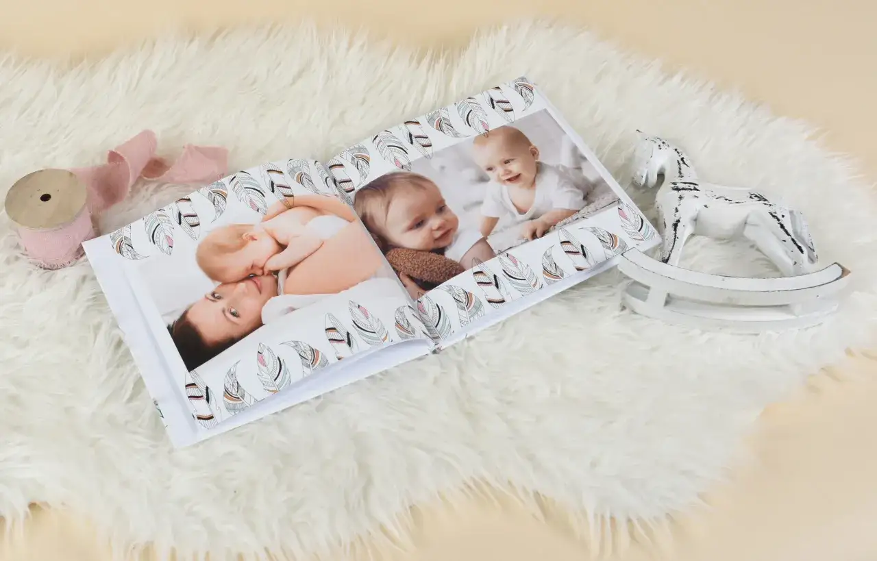 Otwarta fotoksiążka z maluchami i mamą, ozdobiona piórkami. Idealna pamiątka, gratulacje z okazji urodzin dziecka!