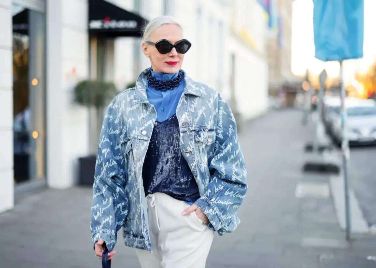 Kobieta w oversize'owej jeansowej katanie z nadrukiem, niebieskiej koszuli i błyszczącym topie.