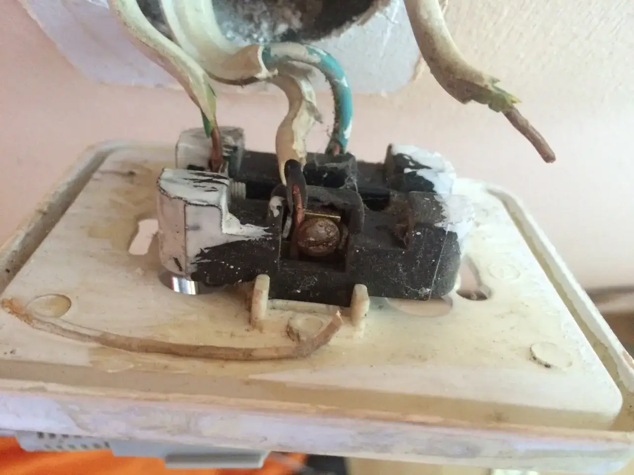 Widok z bliska na rozmontowane gniazdko elektryczne z widocznymi przewodami.