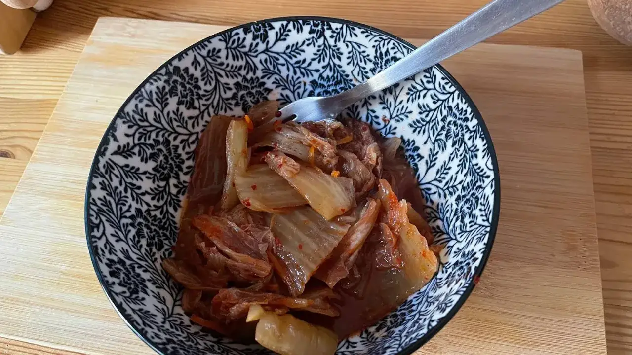 Miseczka z domowym kimchi, widelcem, na drewnianej desce.