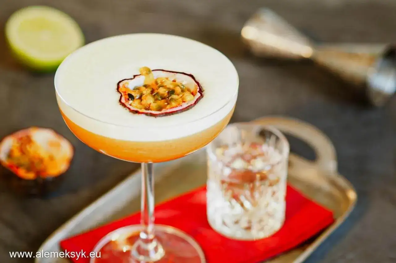 Pyszny drink Pornstar Martini z pianką i owocem marakui, obok kieliszek z drinkiem i połówka limonki.