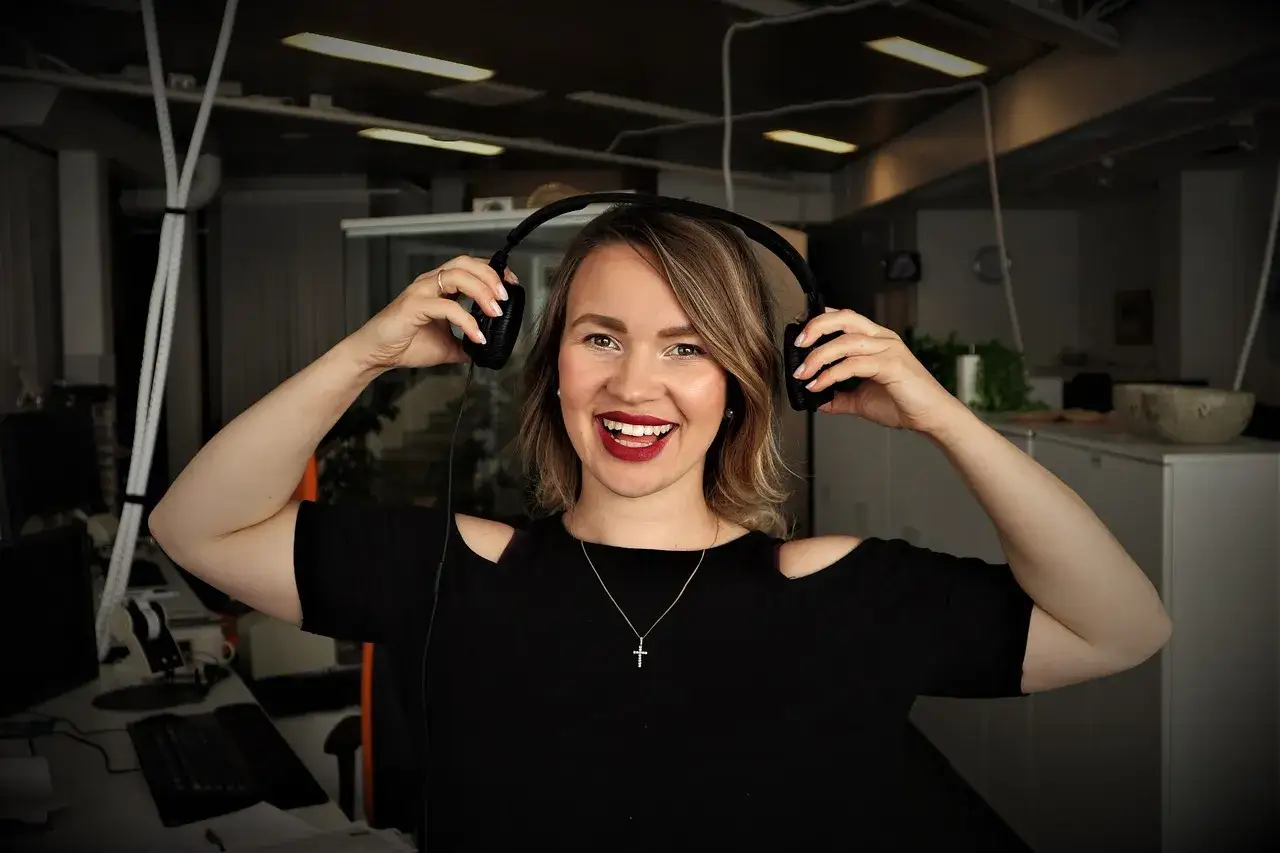 Uśmiechnięta kobieta z słuchawkami na uszach, słucha podcastów do nauki angielskiego.