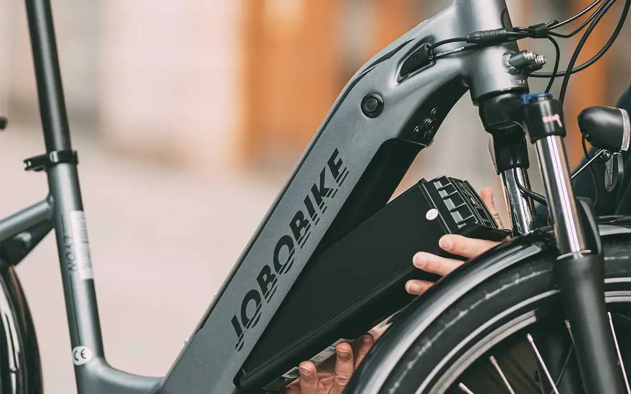Ręce wyjmujące czarną baterię z ramy roweru elektrycznego JOBORBIKE.