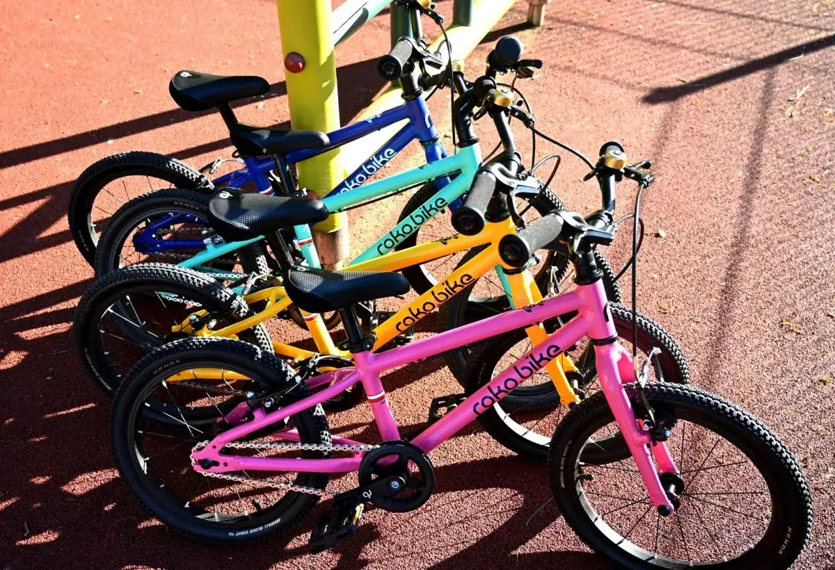 Rowerki dziecięce roko bikes w kolorach: różowym, żółtym, turkusowym i niebieskim, gotowe do zabawy na placu.
