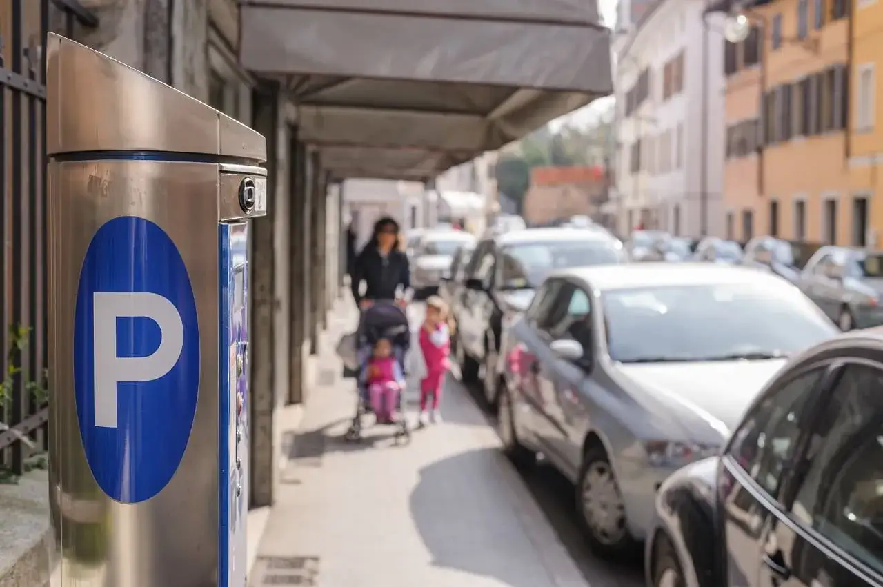 Parkomat z symbolem "P" i w tle kobieta z dziećmi na wózku, a obok samochody. Czy to parkowanie w miejscu niedozwolonym?