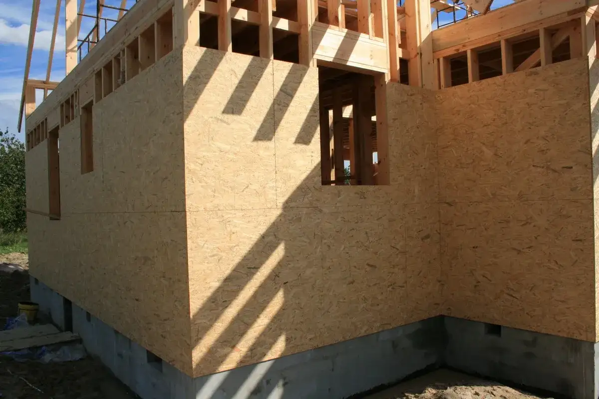 Budowa domu, ściany zewnętrzne z płyt OSB, widoczne okna i fundament.