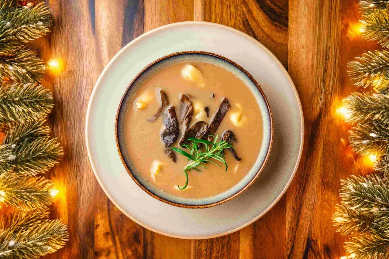 Zastanawiasz się, co podać na świąteczny obiad? Aromatyczna zupa grzybowa z ziemniakami i gałązką rozmarynu, otoczona świątecznymi iluminacjami.