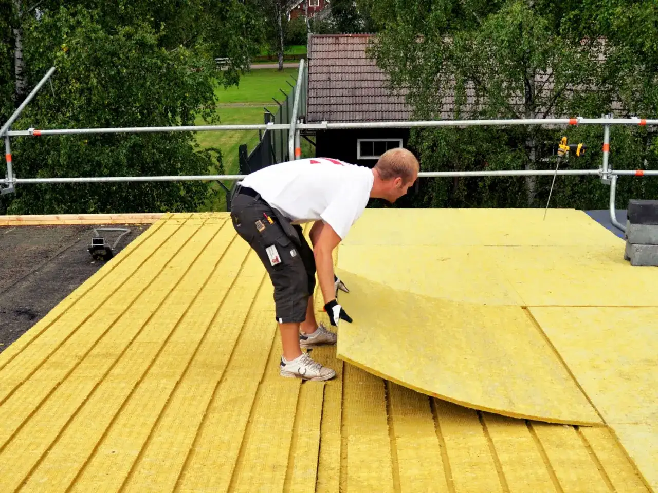 Pracownik układa płyty izolacyjne na dachu płaskim. Zapewnia to skuteczną izolację termiczną budynku.
