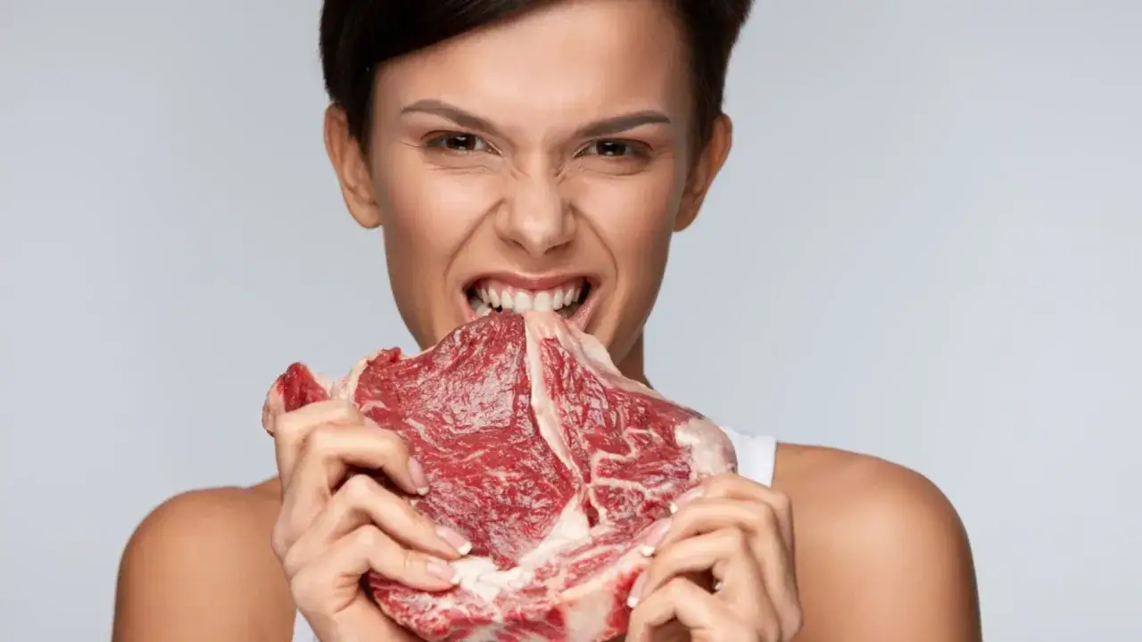 Kobieta z dziką miną wgryza się w surowy kawałek mięsa. Czy można brać białko bez treningu?