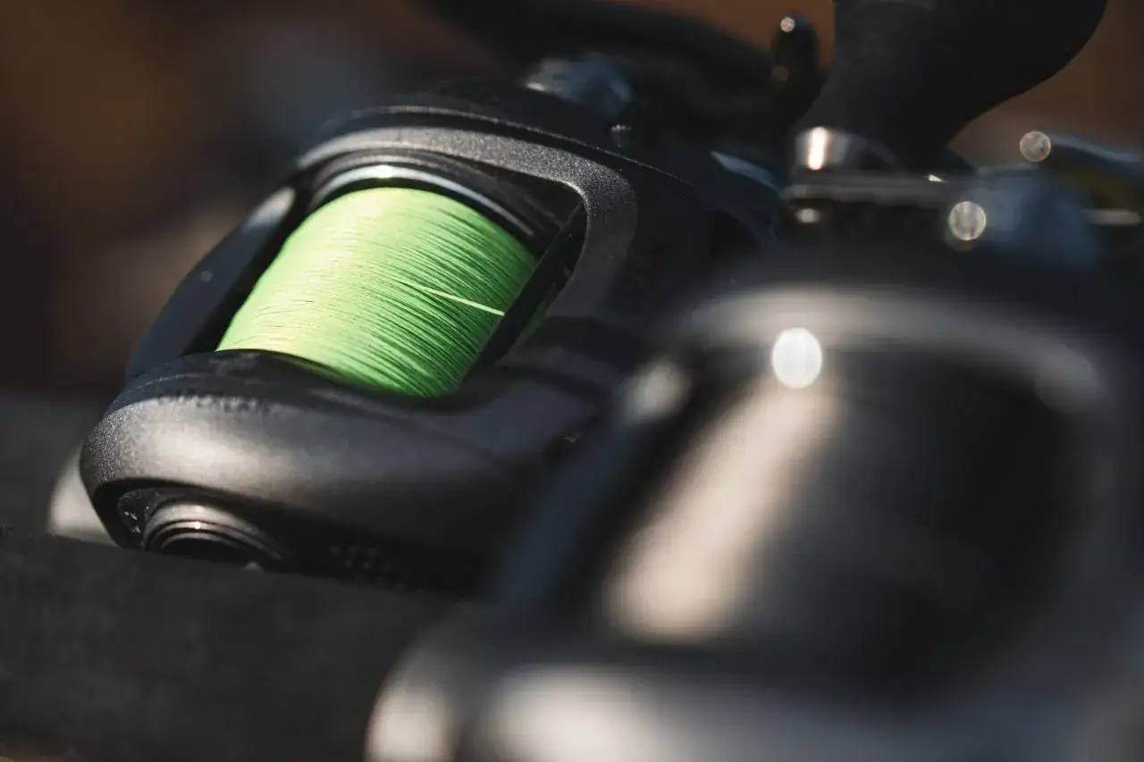 Zbliżenie na kołowrotek spinningowy z nawiniętą zieloną plecionką.