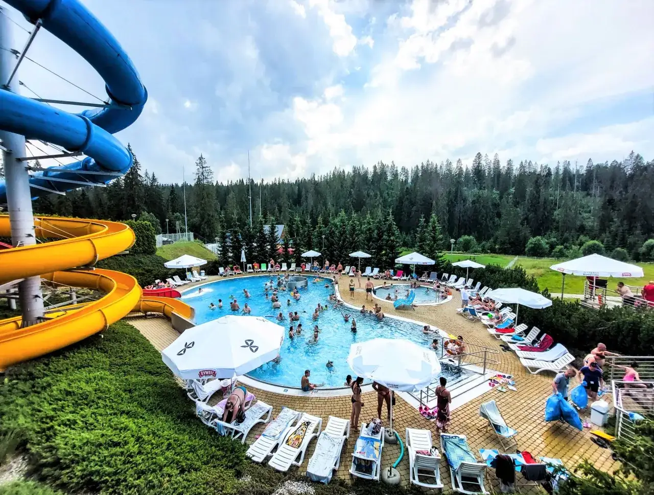 Aqua park Bukowina tętni życiem. Ludzie kąpią się w basenie, zjeżdżają ze zjeżdżalni i odpoczywają na leżakach.