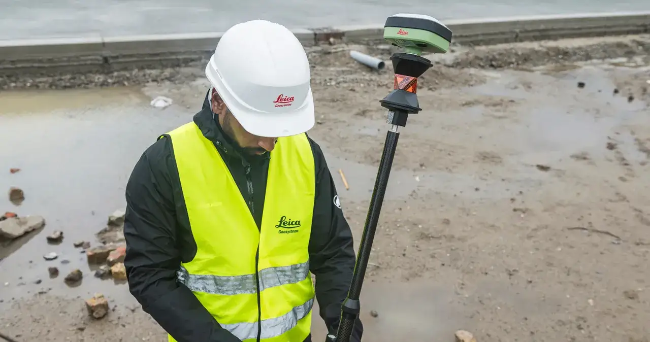 Geodeta w kamizelce odblaskowej i kasku z instrumentem Leica na budowie.