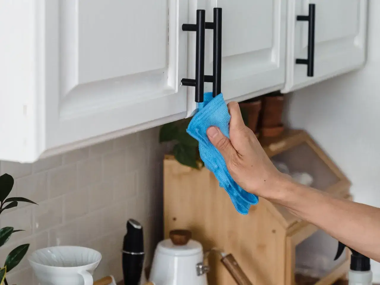 Ręka z niebieską ściereczką czyści uchwyt szafki, docierając do ukrytych siedlisk bakterii w kuchni, o których zapominasz przy porządkach.