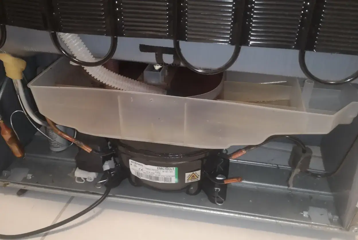 Widok wnętrza lodówki Whirlpool z widocznym kompresorem i tacą skraplacza.