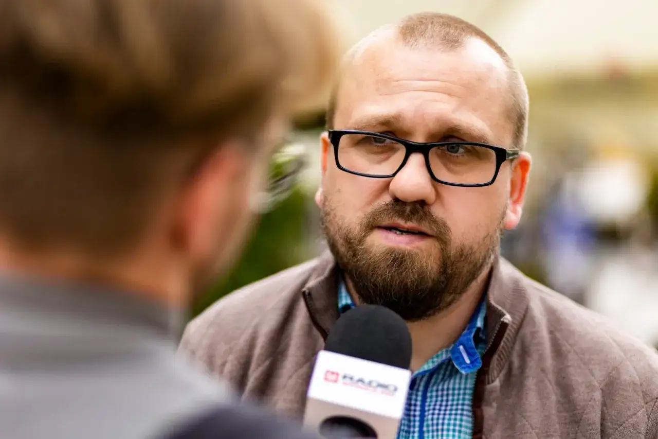 Mężczyzna w okularach udziela wywiadu mikrofonowi radiowemu.