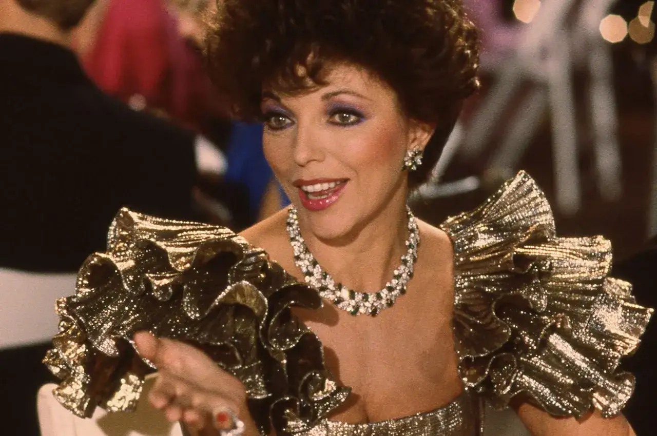 Alexis z Dynastii w olśniewających, złotych strojach z falbanami i biżuterią.