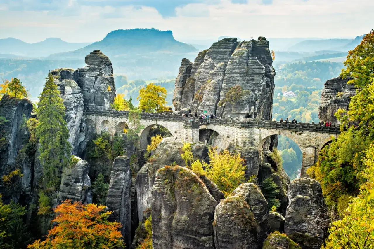 Most Bastei, skalne miasto w Saksonii, z kamiennym mostem łączącym skalne iglice. Jesienne liście dodają koloru krajobrazowi.