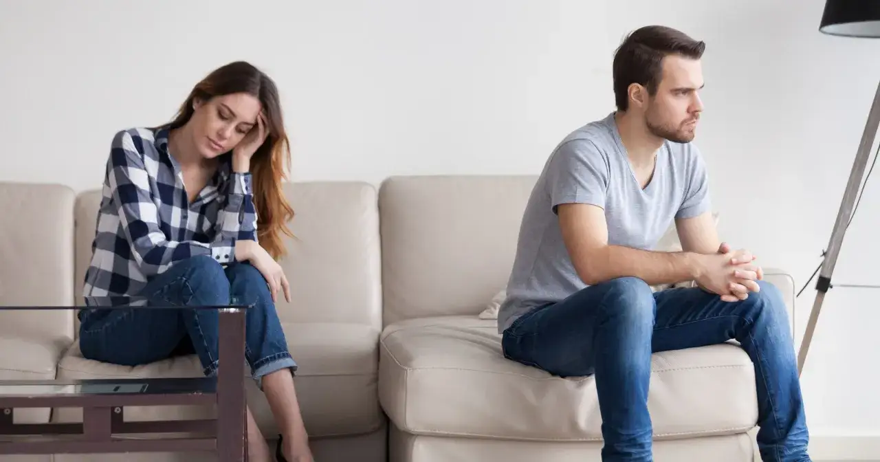 Para, siedząca na kanapie, zamyślona, zastanawia się, jak przeprosić faceta sms. On siedzi obok, odwrócony.