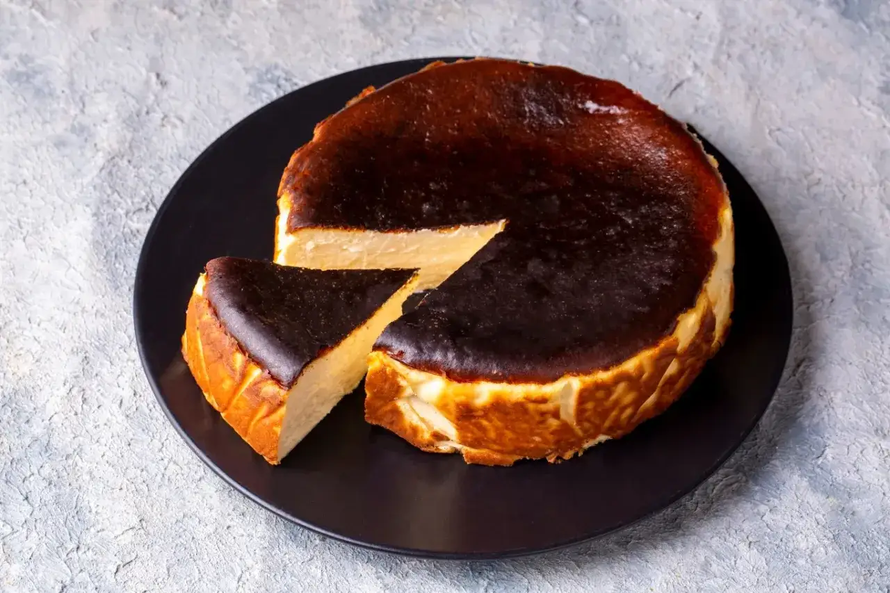 Pyszny, lekko przypieczony sernik na czarnym talerzu. Widać, ile piec sernik był idealnie wypieczony.