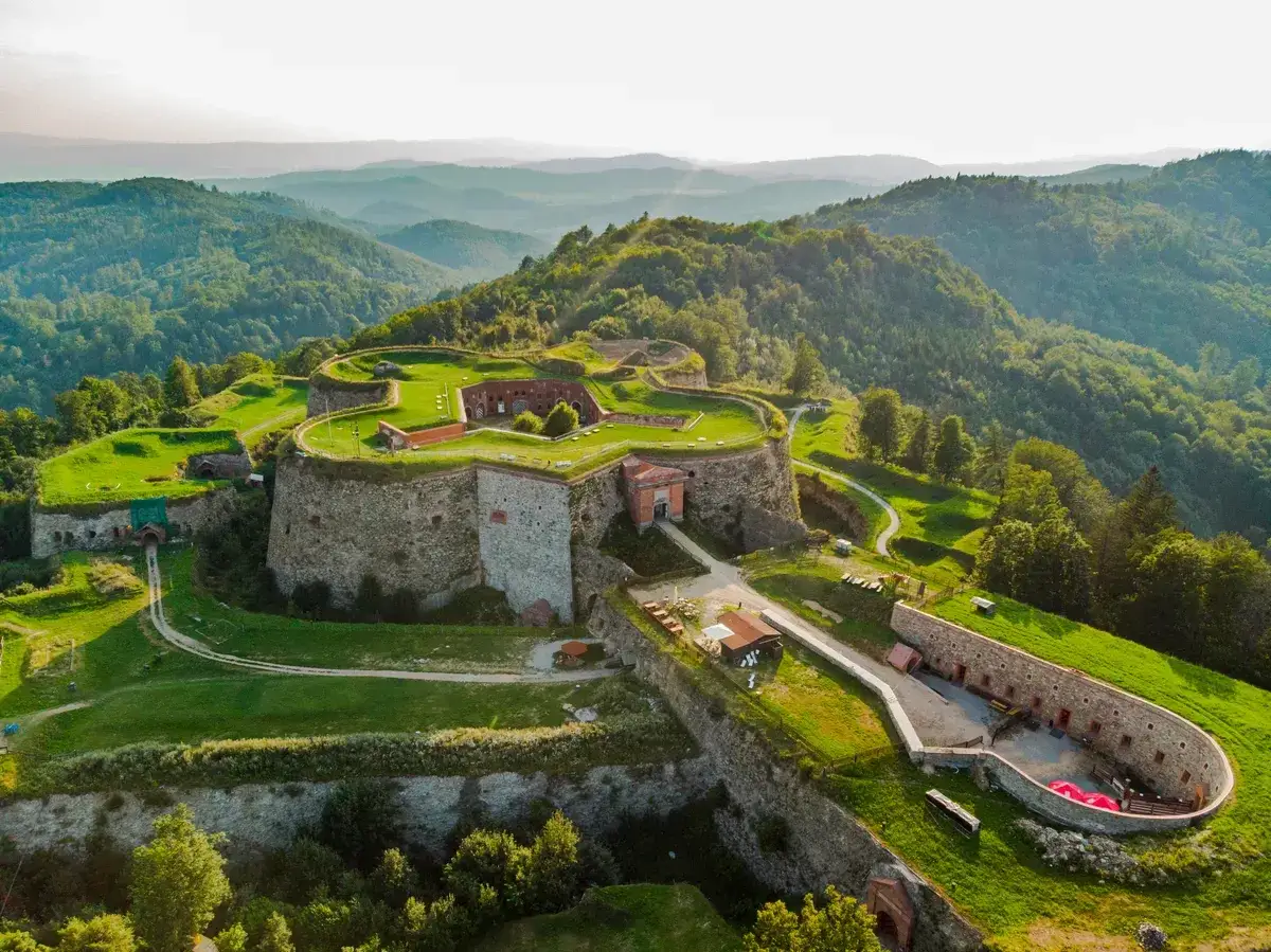 Forteca na wzgórzu, otoczona zielenią, z widokiem na góry. Srebrna góra trasa zaprasza do odkrywania historii.