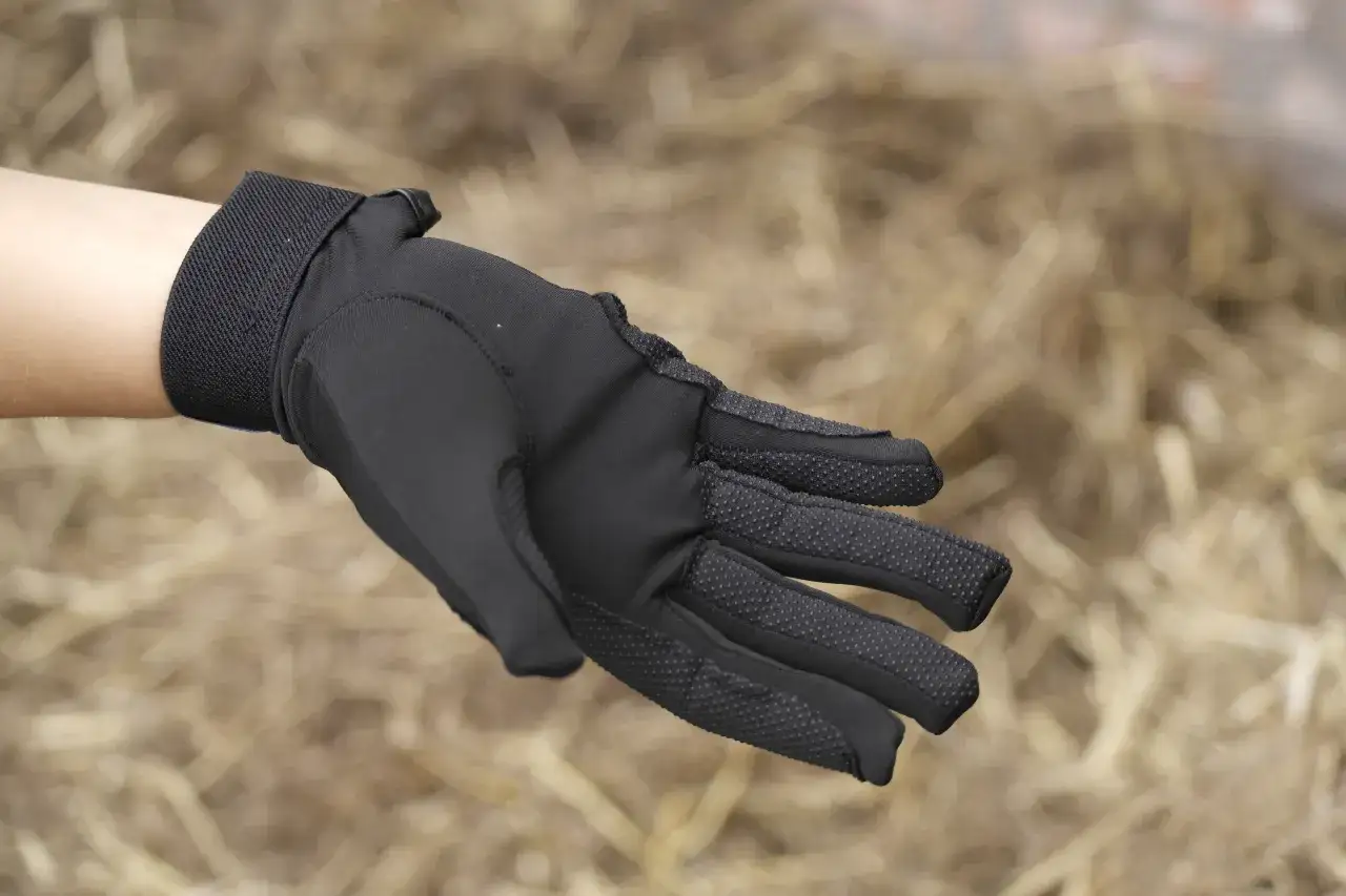 Dłoń w czarnej rękawiczce jeździeckiej z antypoślizgowymi wypustkami na palcach.