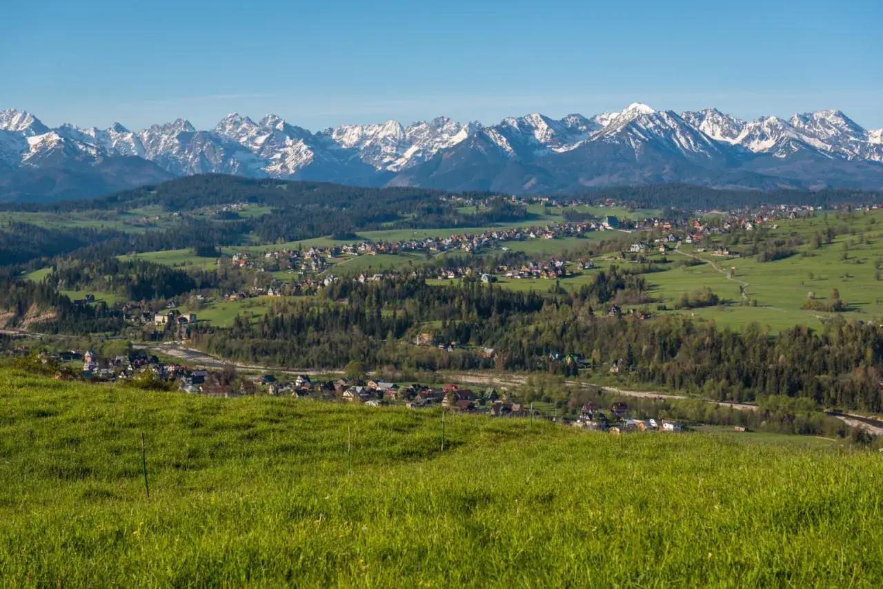 Widok na Tatry z zielonych wzgórz. W oddali widać zabudowania, które mogą być częścią trasy, ile km z Zakopanego do Bukowiny Tatrzańskiej.