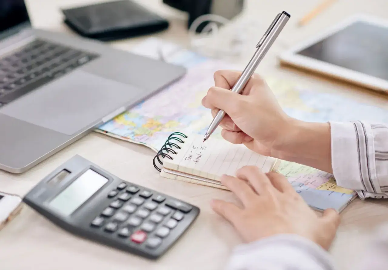 Osoba notuje na zeszycie, jak obliczyć odsetki od pożyczki prywatnej, obok leży kalkulator i laptop.
