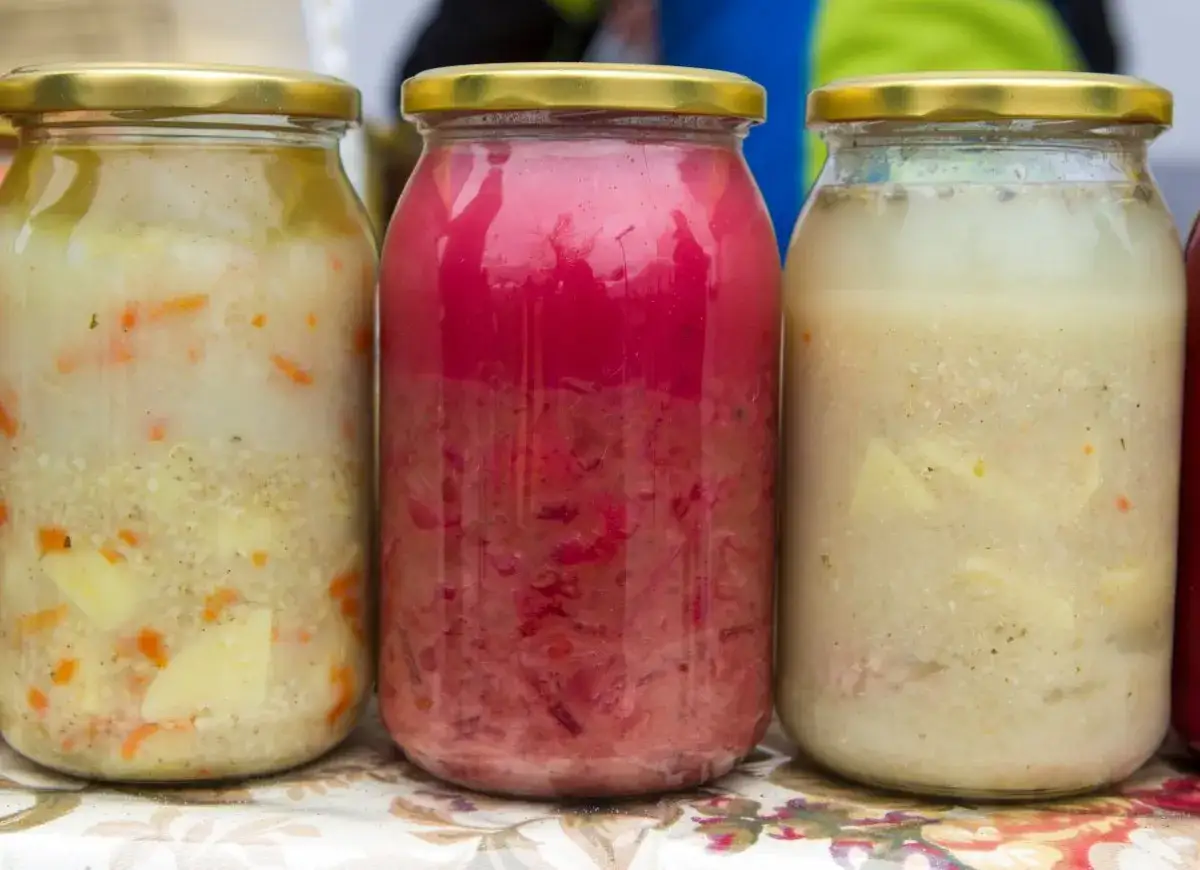 Trzy słoiki z zupami: jedna różowa, dwie kremowe z warzywami.