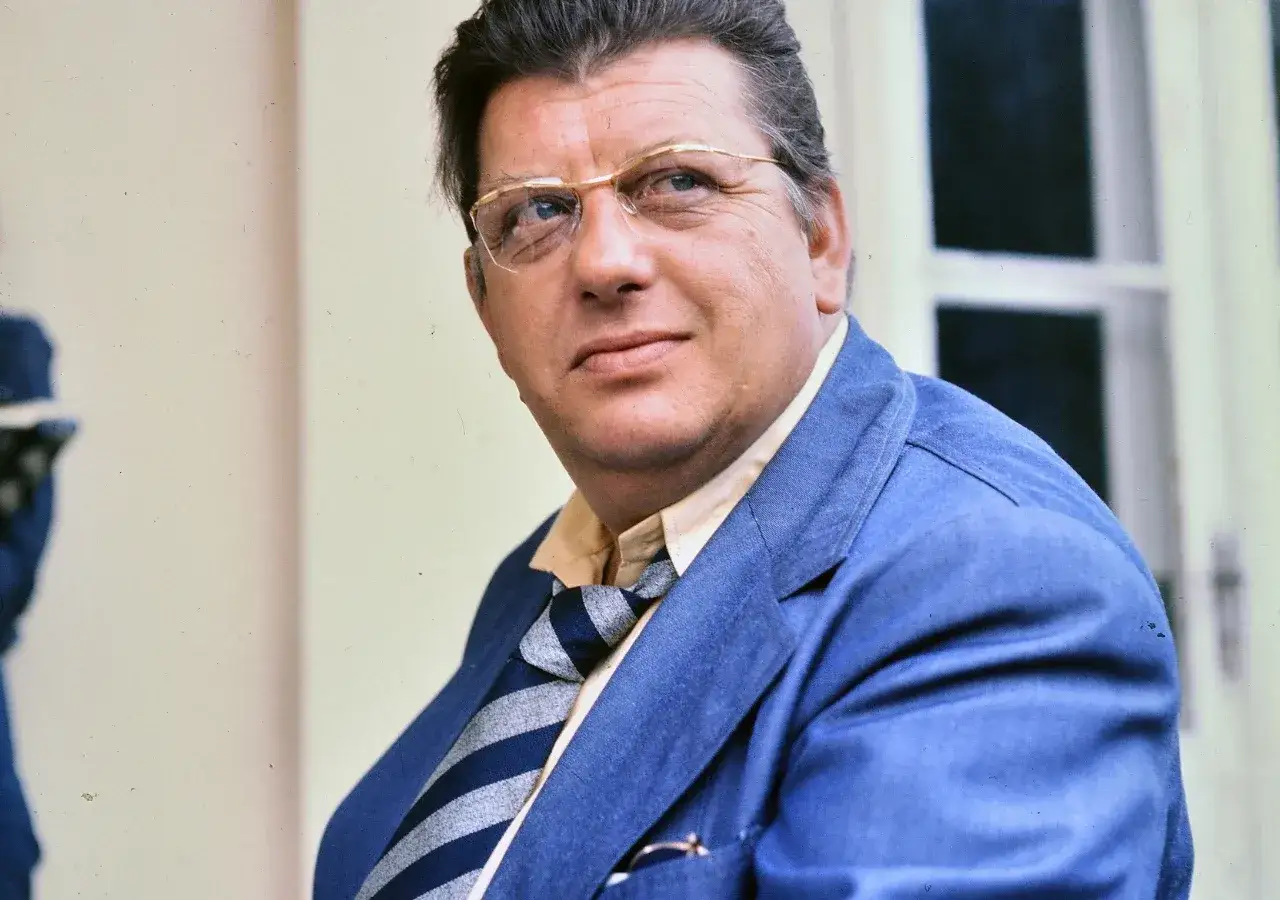 Portret Mariusza Dmochowskiego w okularach i niebieskiej marynarce. W tle okno.