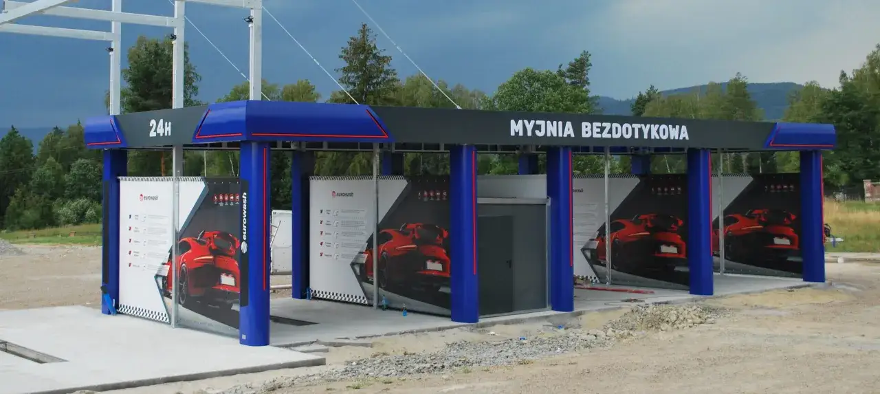 Nowoczesna myjnia bezdotykowa z niebieskimi elementami i reklamami czerwonych samochodów.