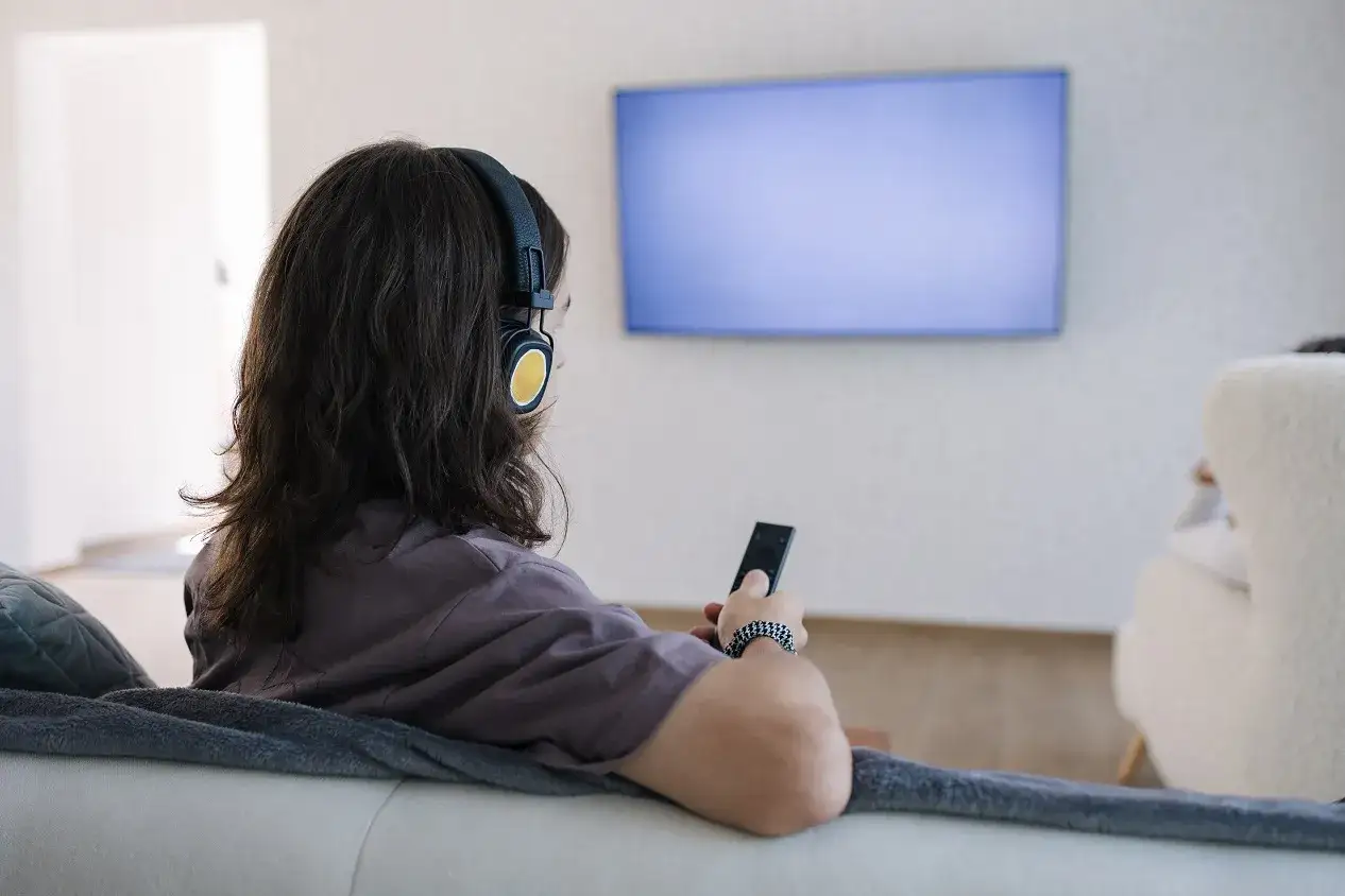 Osoba w słuchawkach z pilotem w ręku, szuka sposobu, jak podłączyć słuchawki bezprzewodowe do telewizora bez bluetooth.