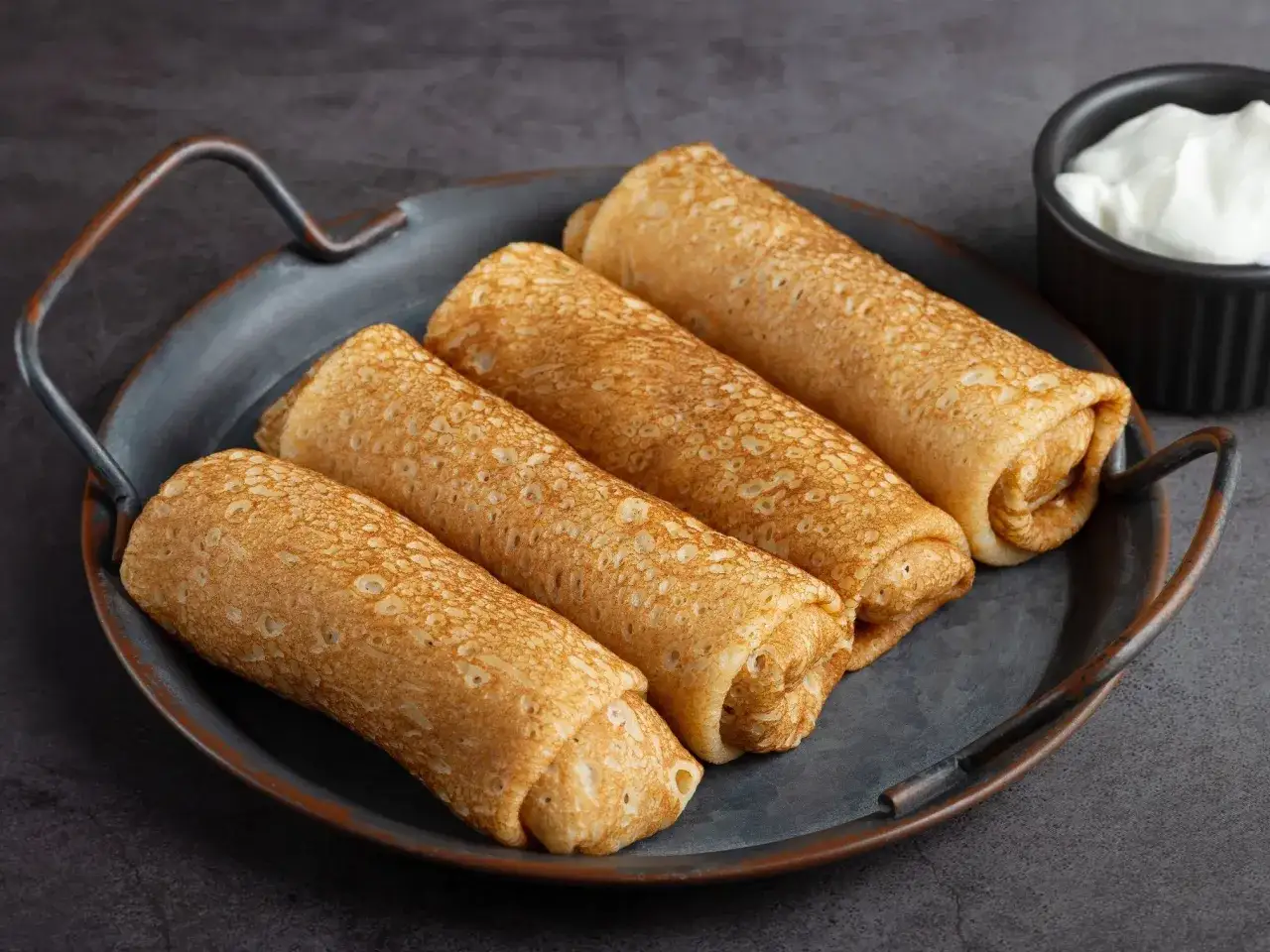 Z czym podać krokiety na obiad? Na tacy leżą złociste krokiety, obok miseczka ze śmietaną.