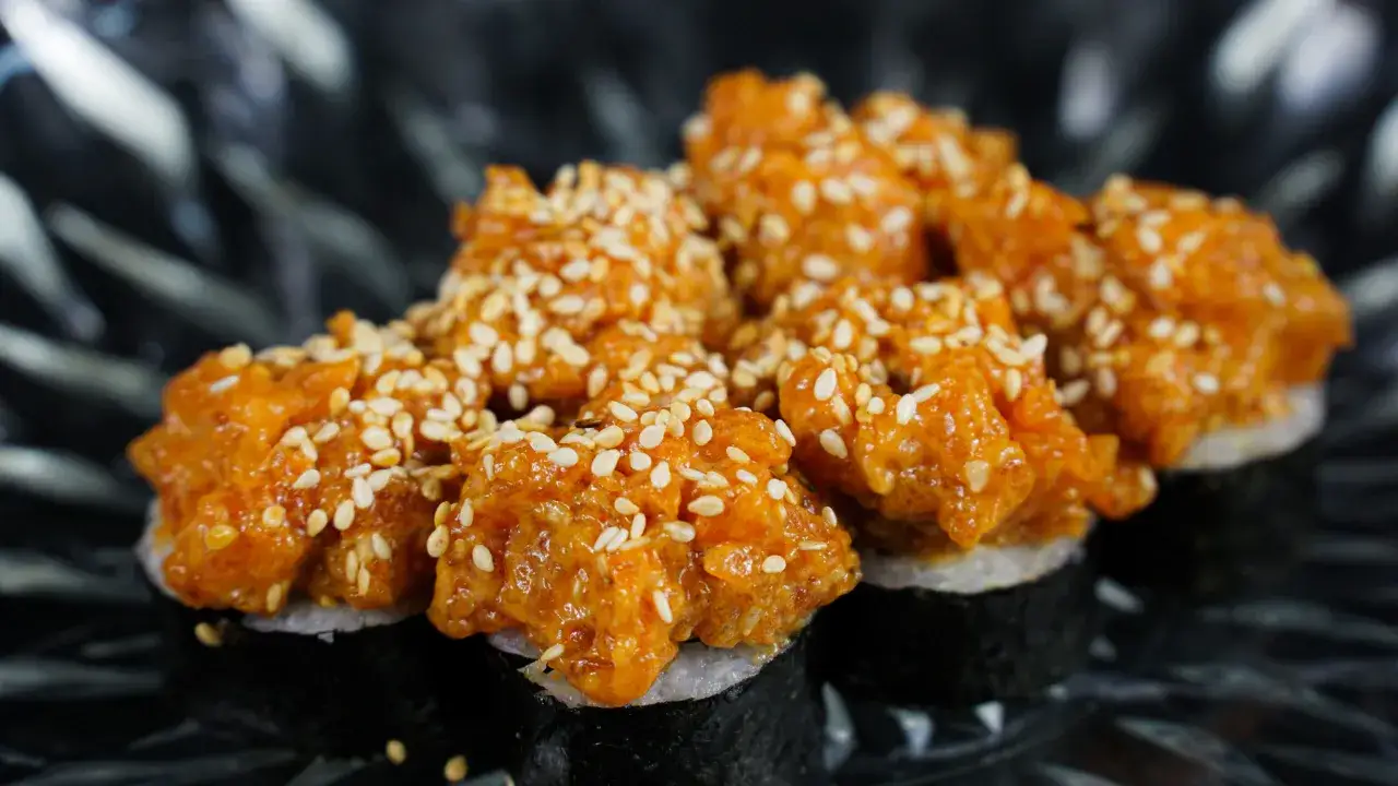 Pyszne sushi z tatarem z łososia, posypane sezamem, prezentuje się apetycznie na ciemnym talerzu.