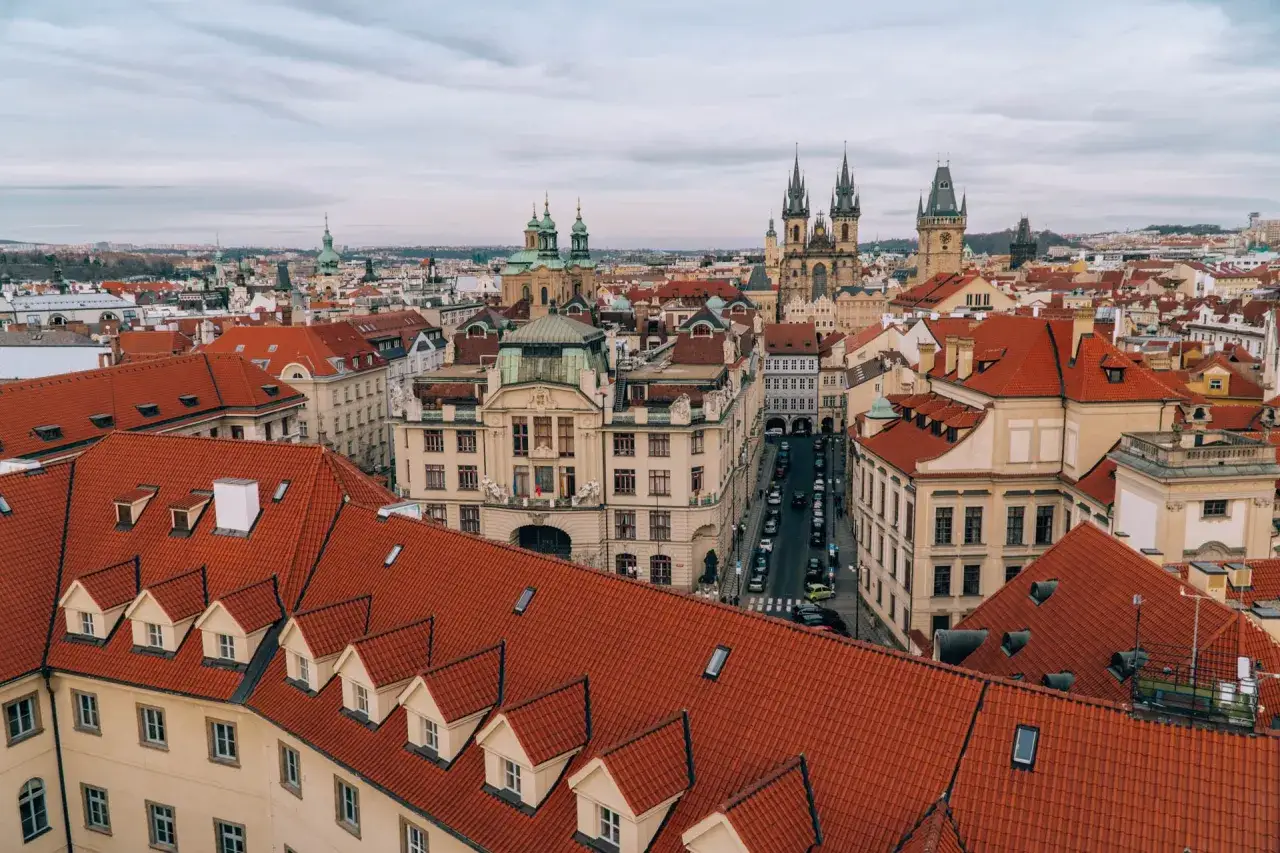 Widok na dachy Pragi, z widocznymi wieżami kościołów i ulicą z samochodami, gdzie porusza się komunikacja miejska.