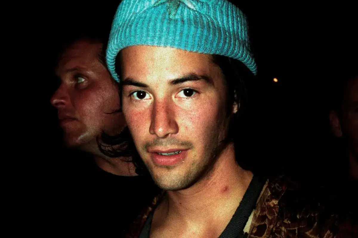 Młody Keanu Reeves w niebieskiej czapce, obok niego inny mężczyzna. Trudno zgadnąć, ile lat ma Keanu Reeves na tym zdjęciu.
