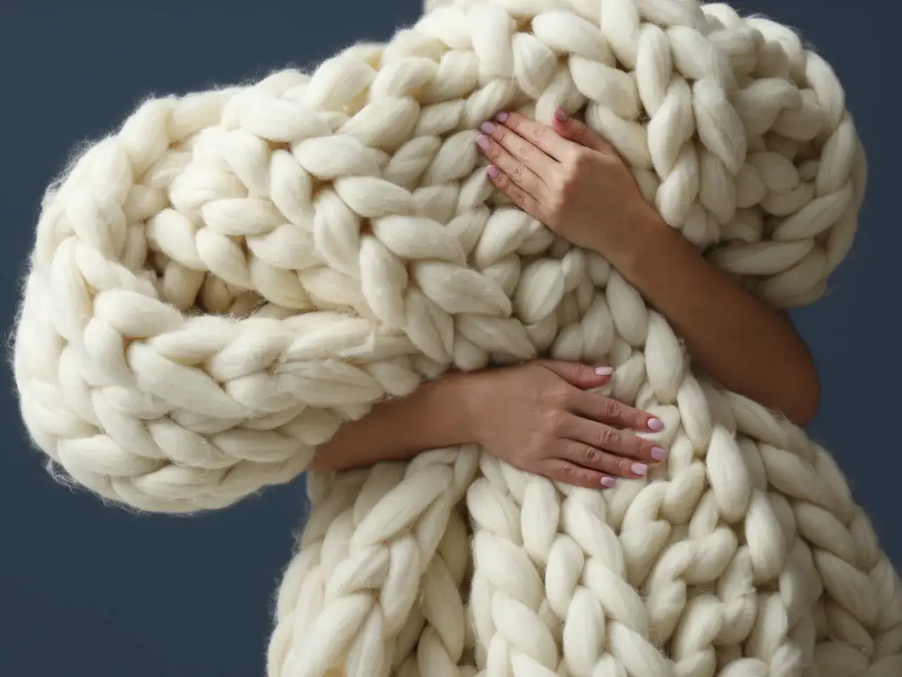 Dłonie otulone grubym, kremowym splotem z wełny czesankowej. Miękkość i ciepło w czystej postaci.