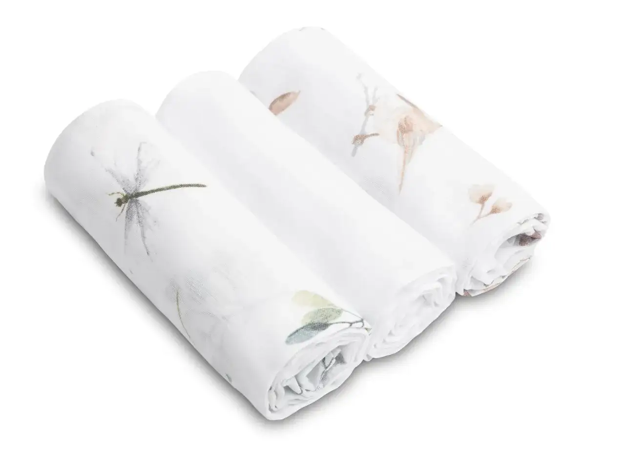 Trzy białe pieluchy muślinowe z delikatnymi wzorami: ważka, ptaszek i liście.