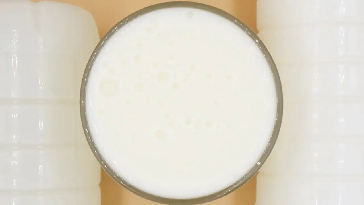 Szklanka pełna pianistego kefiru, otoczona białymi butelkami. Idealny moment, kiedy pić kefir, to teraz!