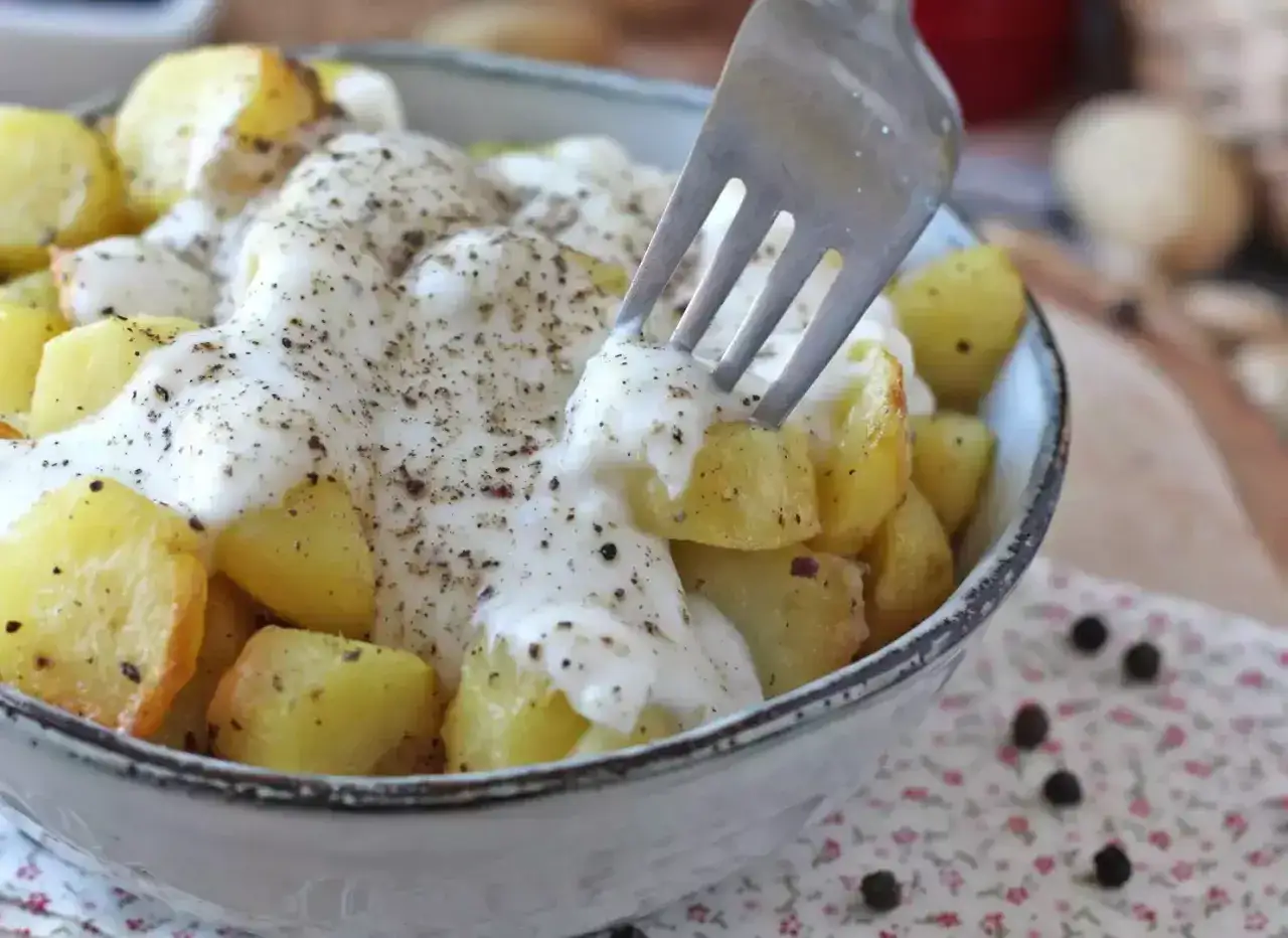 Ziemniaki w kremowym sosie z pieprzem, inspirowane przepisem Cacio e Pepe. Widok z bliska na widelec nabijający ziemniaka.