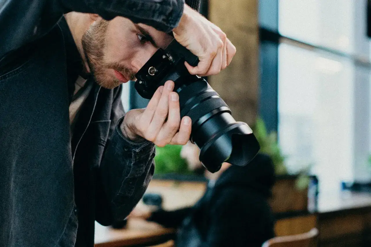 Mężczyzna z brodą w czarnej kurtce trzyma aparat, gotowy do uchwycenia chwili w stylu street photography.