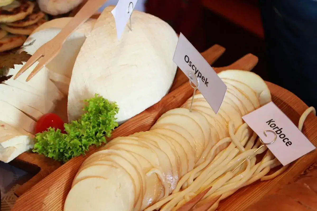 Różne rodzaje serów, w tym oscypek i korboce, na drewnianej desce z dekoracjami.