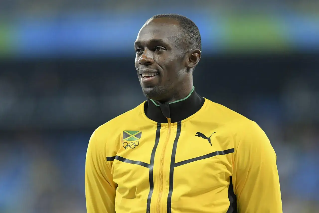 Usain Bolt w żółtej kurtce z flagą Jamajki i logo olimpijskim. Zastanawiasz się, jak szybko biega Usain Bolt?