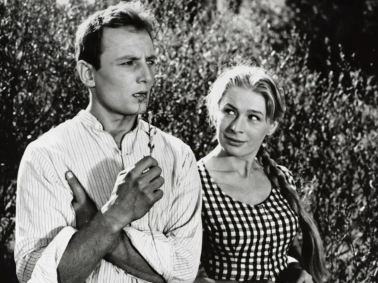 Młody mężczyzna, Eugeniusz Korczarowski, z gałązką w ustach, spogląda w bok. Obok niego uśmiechnięta kobieta w kratkę.